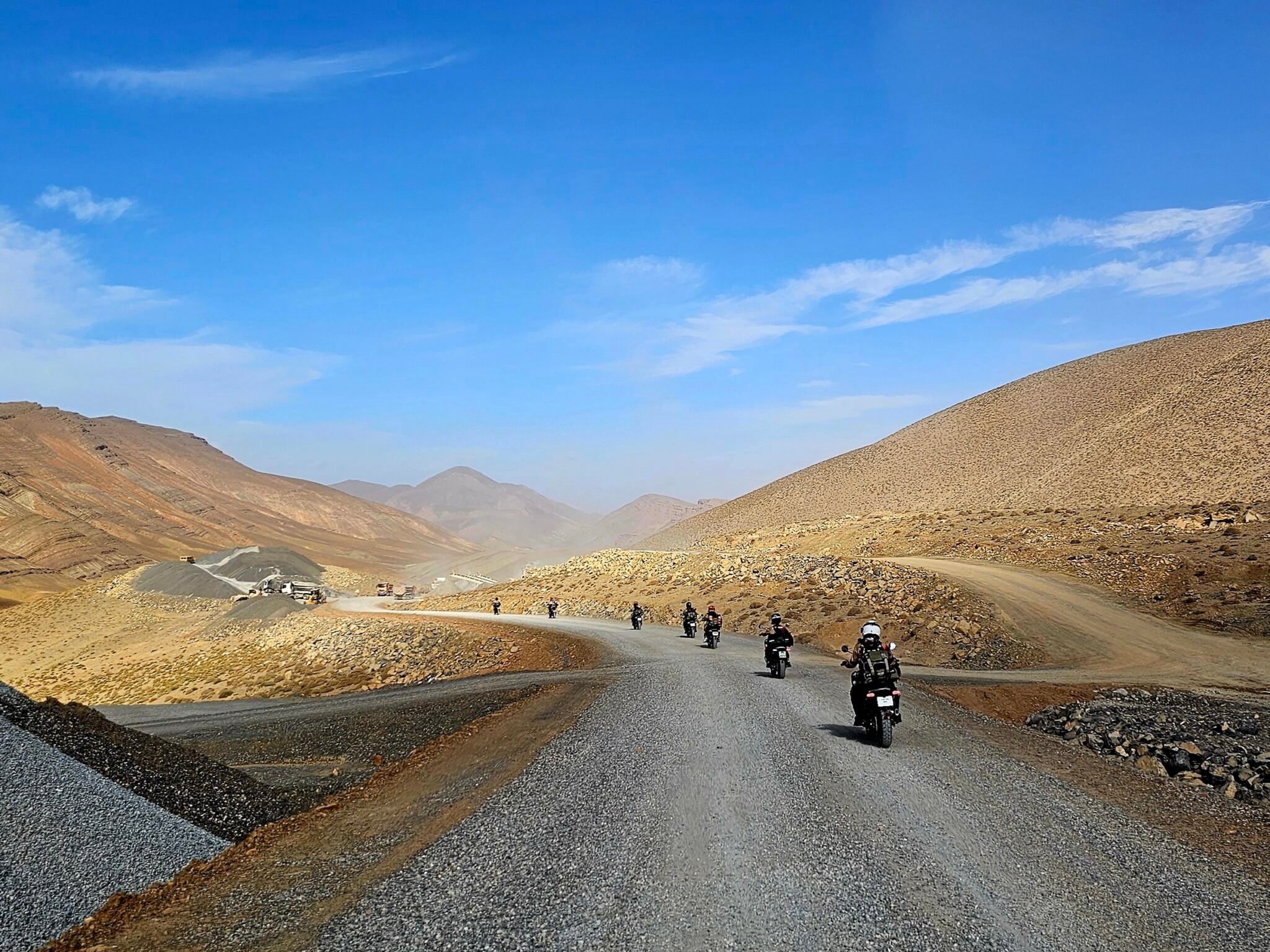 Motorcyclists riding along a winding gravel road through a mountainous landscape under a clear blue sky, showcasing the beauty of adventure travel in nature.