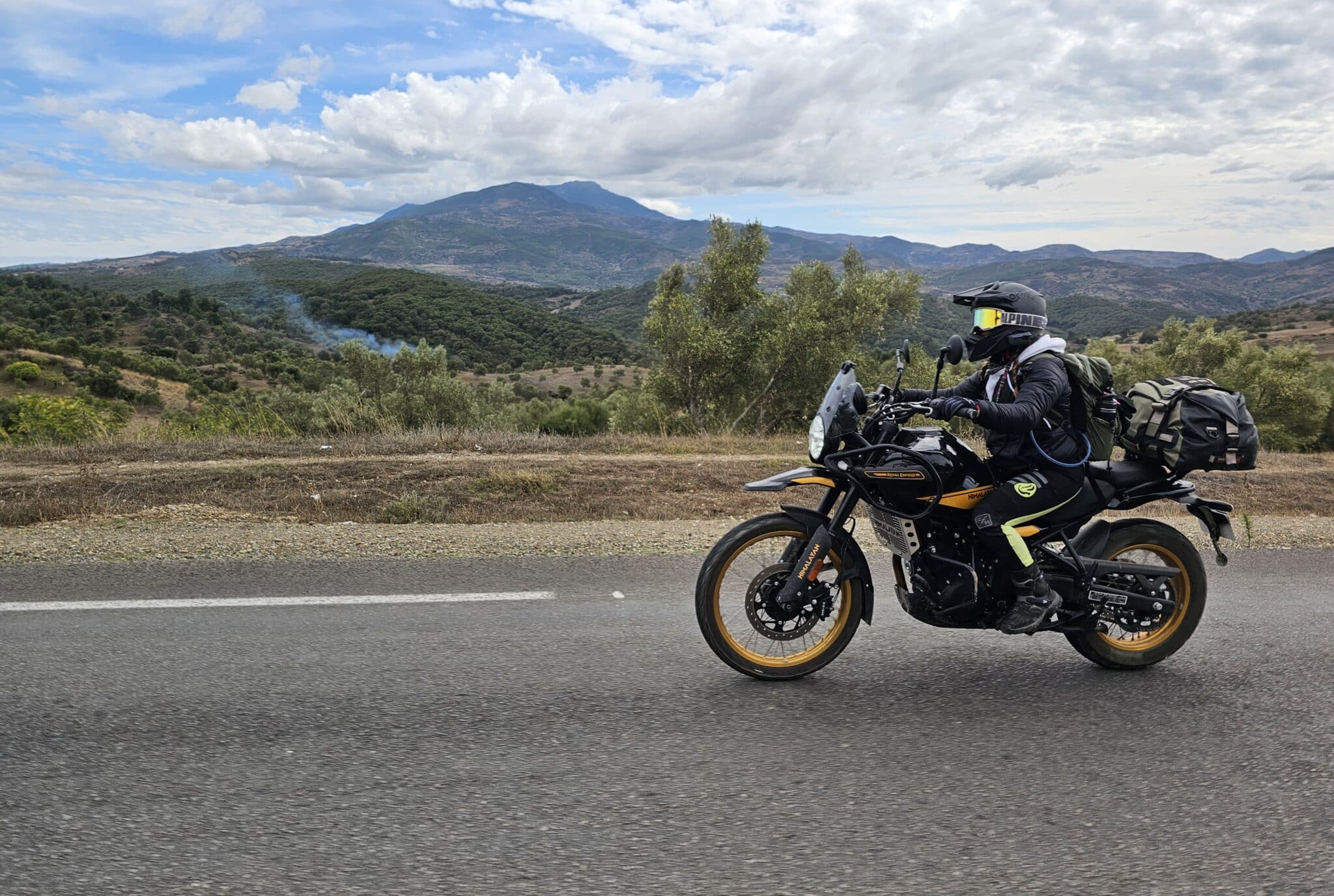 Woman riding a motorcycle with natural scenery all around.