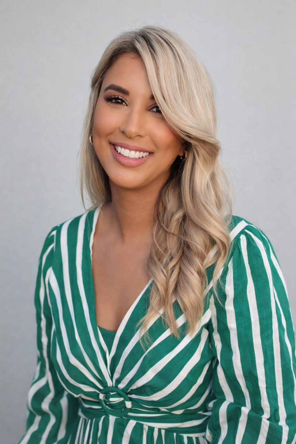 Smiling woman with long blonde hair wearing a green and white striped blouse, posing against a neutral background.