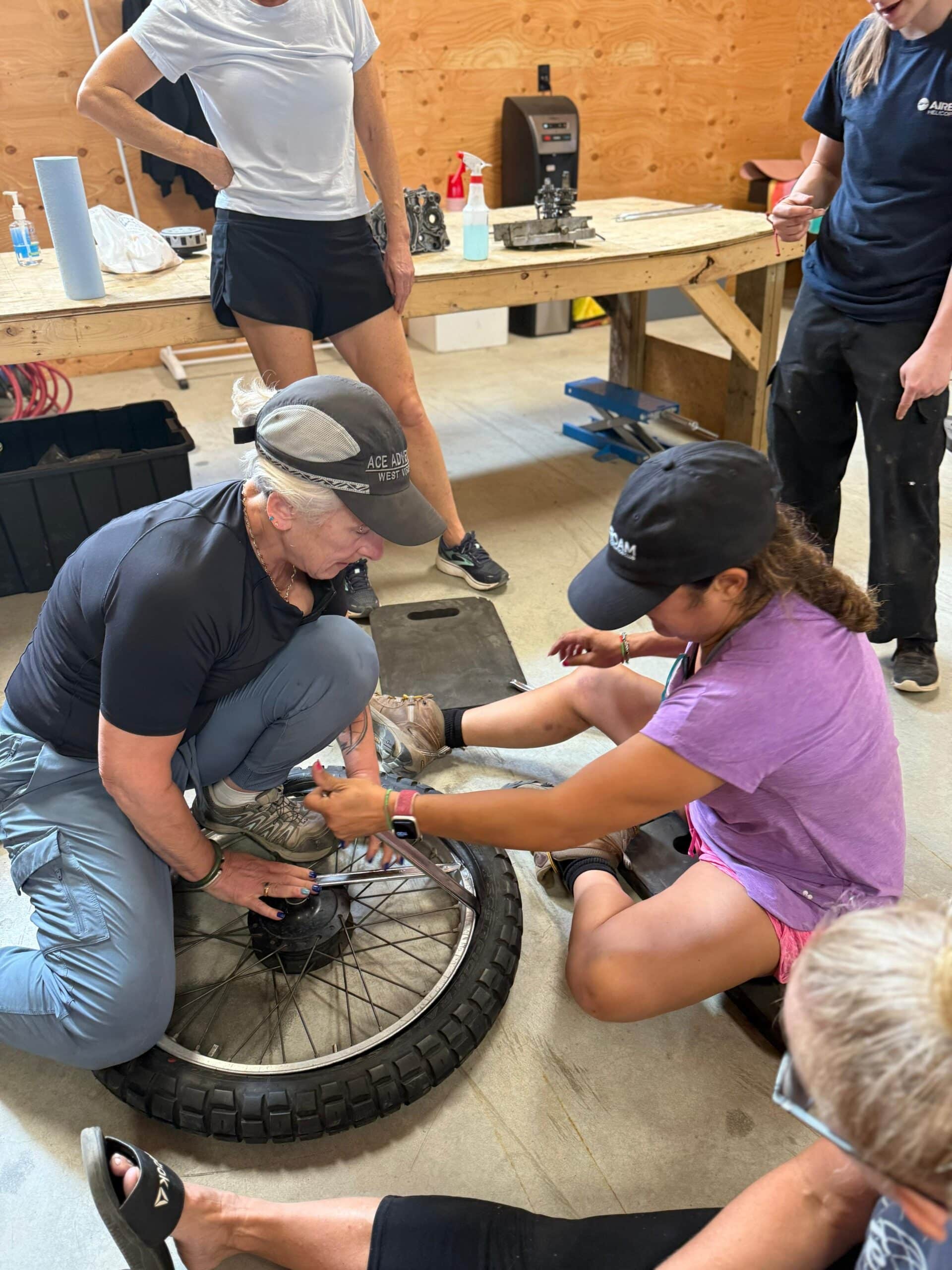 People working together to repair a motorcycle wheel indoors in a workshop.