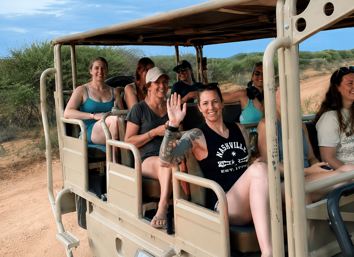Group of women enjoying a safari tour, sitting in an open-air vehicle and smiling, with a scenic landscape in the background.