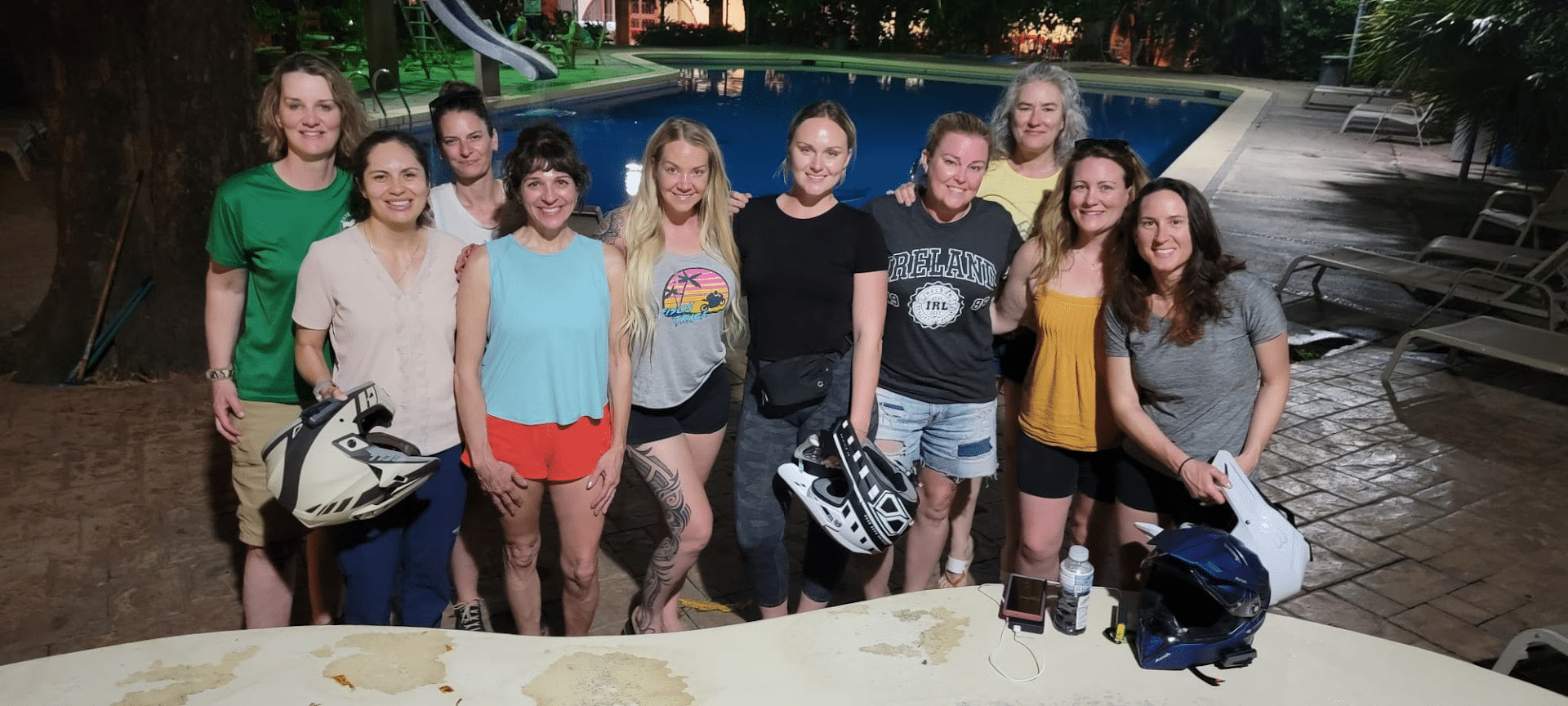 Group of eight women posing together by a pool at night, showcasing a fun and vibrant atmosphere, with a water slide in the background.