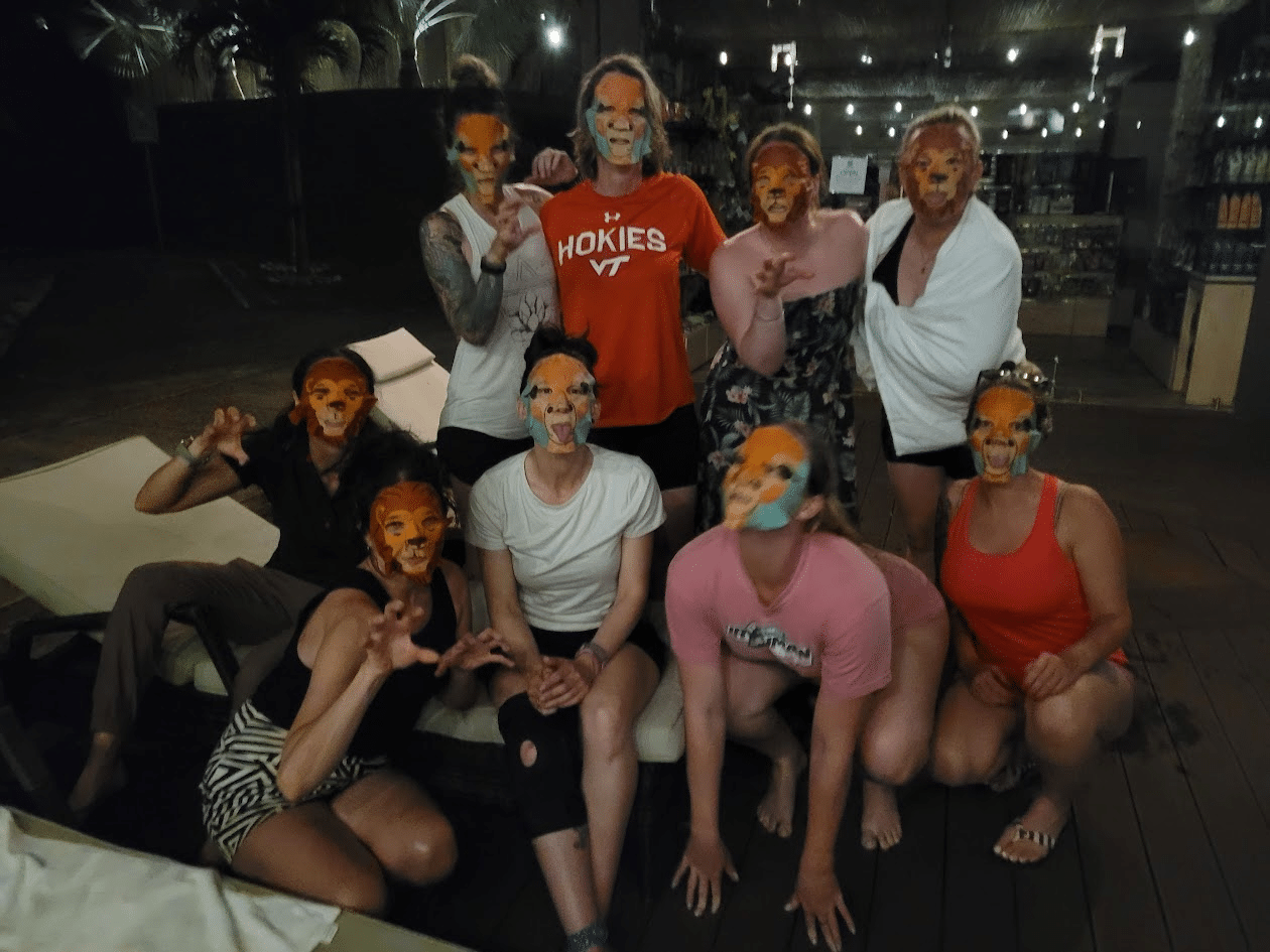 Group of women posing playfully with tiger face masks at a social gathering by a poolside, showcasing a fun and vibrant atmosphere.