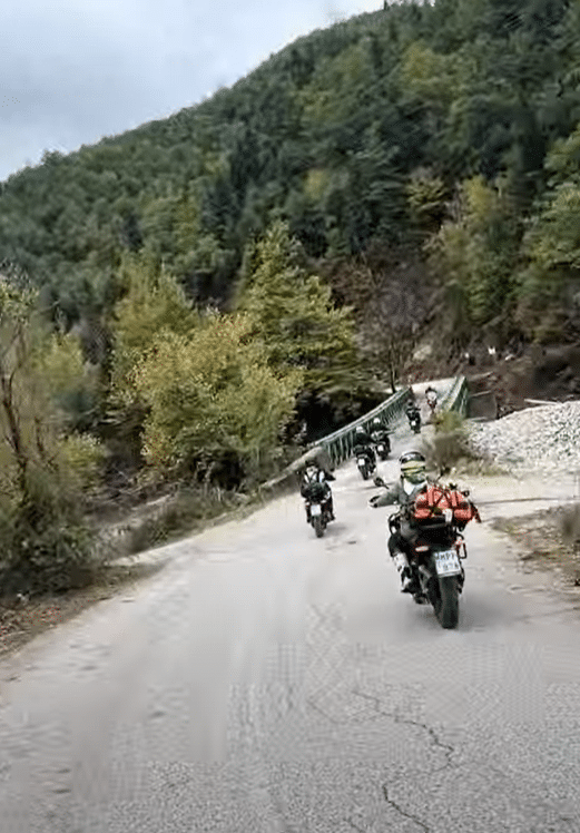 Motorcyclists riding along a scenic mountain road surrounded by lush greenery and autumn foliage.