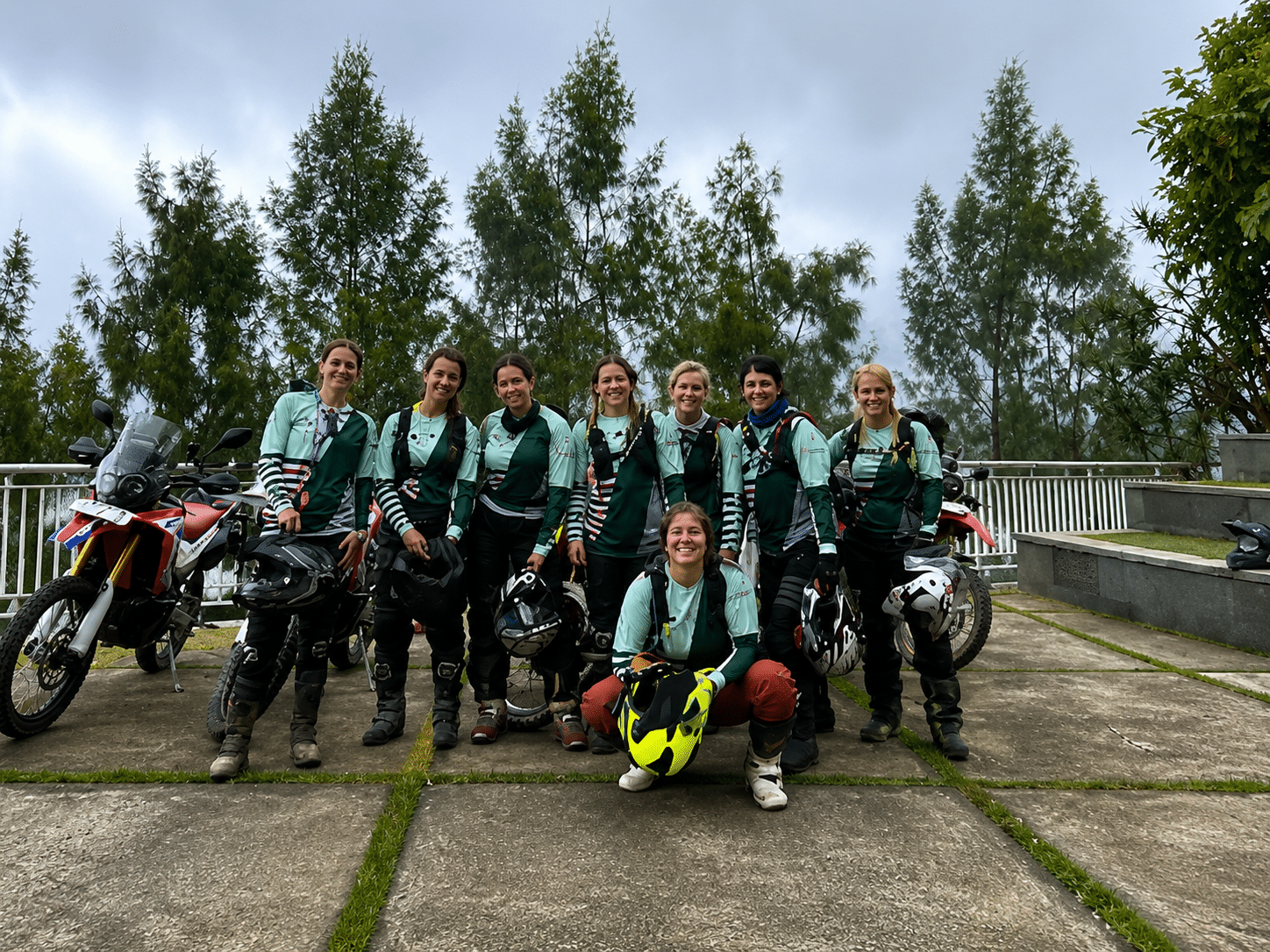 Group of female motorcyclists posing together with their bikes in a foggy outdoor setting, showcasing camaraderie and adventure in a scenic location.