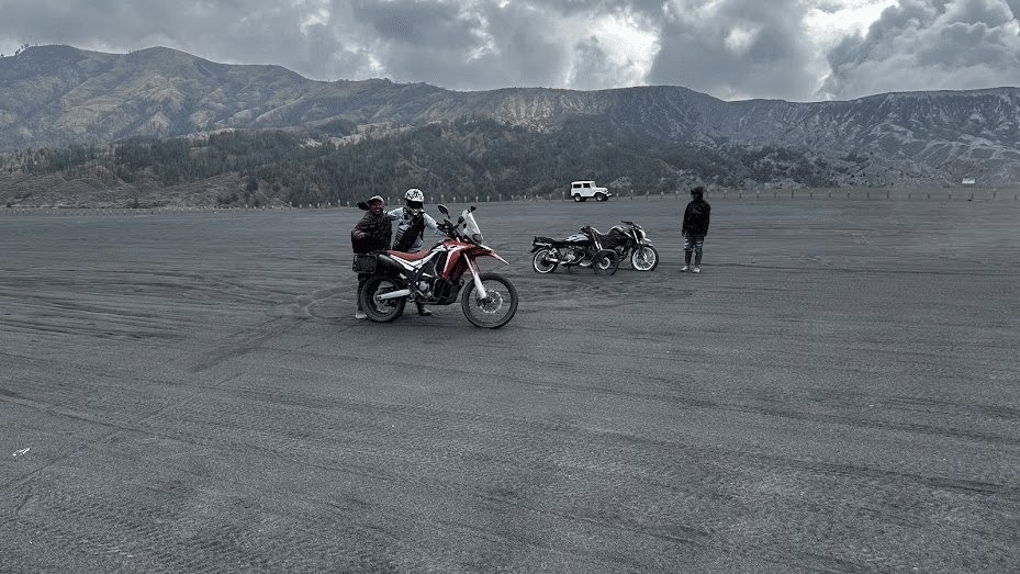 Two motorcyclists on an adventure in a vast, open terrain with mountains in the background, showcasing off-road motorcycles and a cloudy sky.
