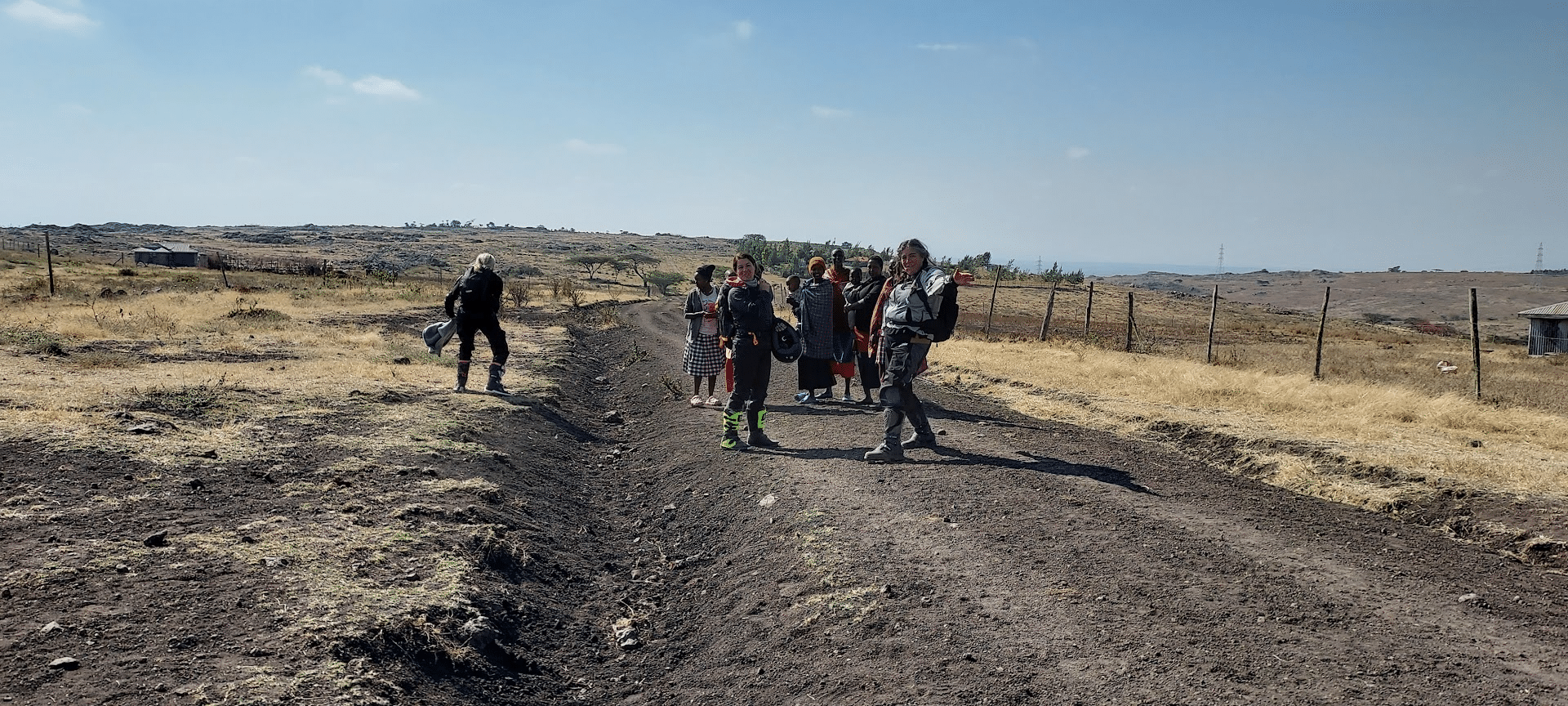 Group of women walking along a dirt path in a rural landscape, with a mix of traditional and modern clothing, surrounded by dry grass and sparse vegetation.