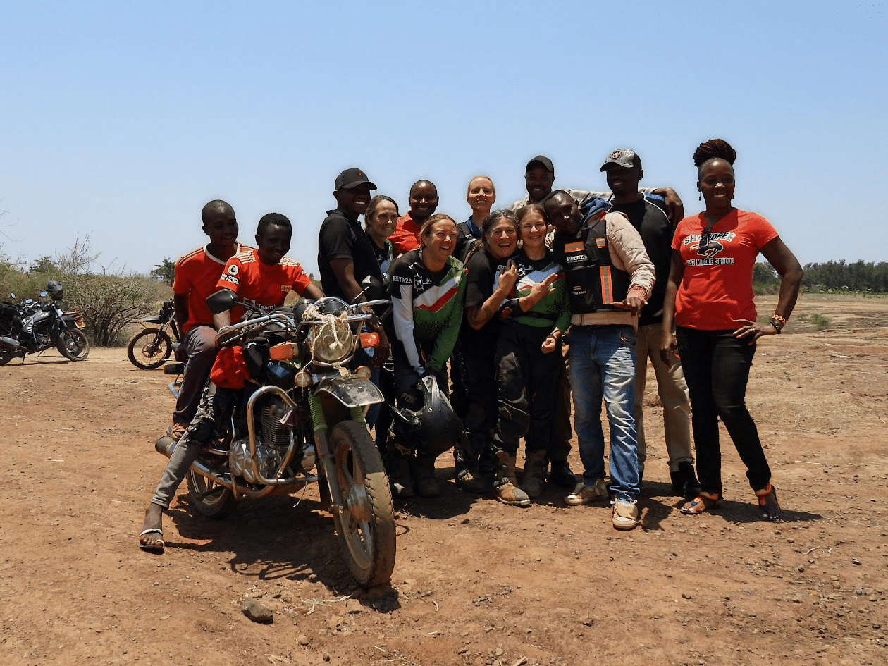 Group of adventure enthusiasts posing with motorcycles in a desert landscape, showcasing camaraderie and outdoor exploration.