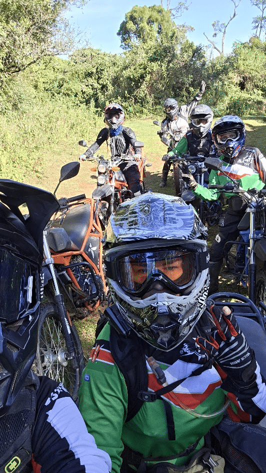 Group of off-road motorcyclists wearing helmets and protective gear outdoors on dirt trail with motorcycles.