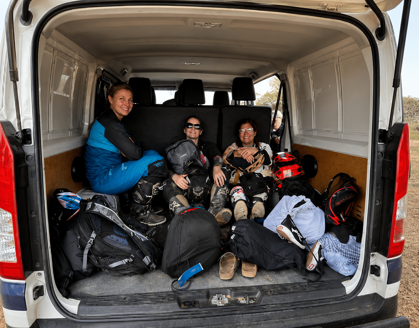 Group of three friends relaxing in the back of a van after a day of outdoor adventure, surrounded by backpacks and gear, showcasing a casual and adventurous lifestyle.