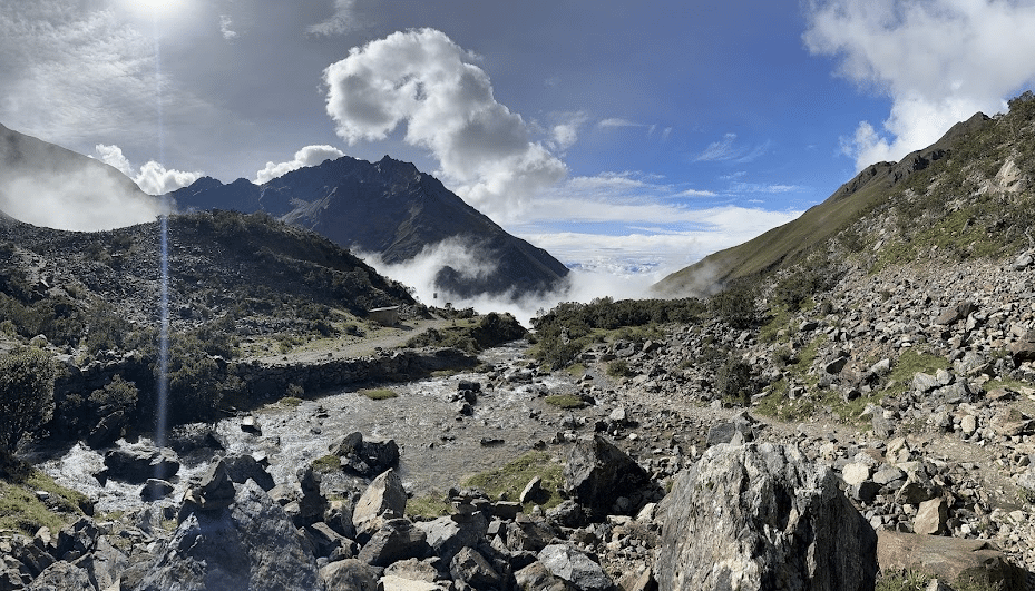 Mountain landscape with rocky terrain, flowing river, and cloudy sky during daytime.
