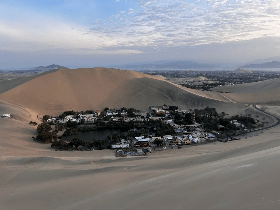 Aerial view of Huacachina oasis village surrounded by sand dunes in the desert at dusk.