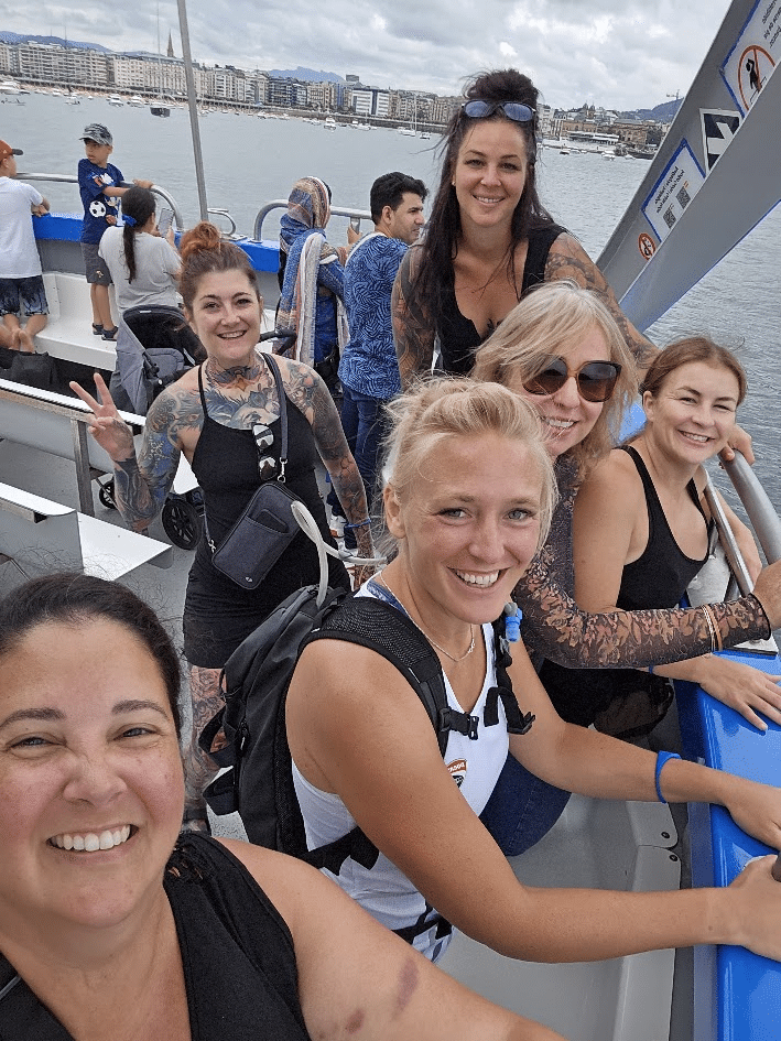 Group of smiling women on a boat with cityscape and water in the background.