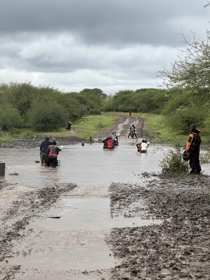People wading through deep water on a dirt trail.