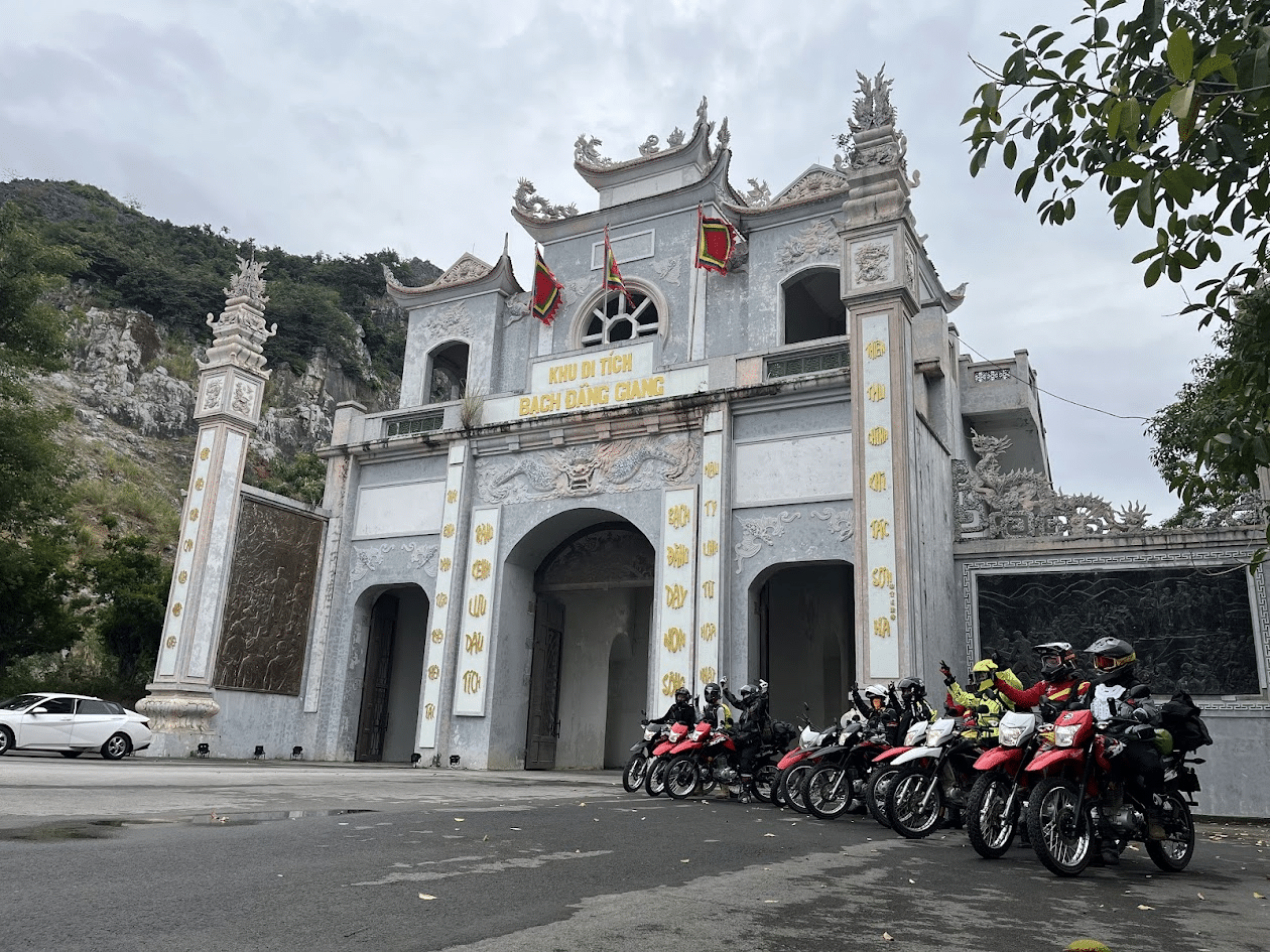 Group of motorcyclists parked in front of the historic Bach Dang Giang gate with traditional Vietnamese architecture and mountainous background.