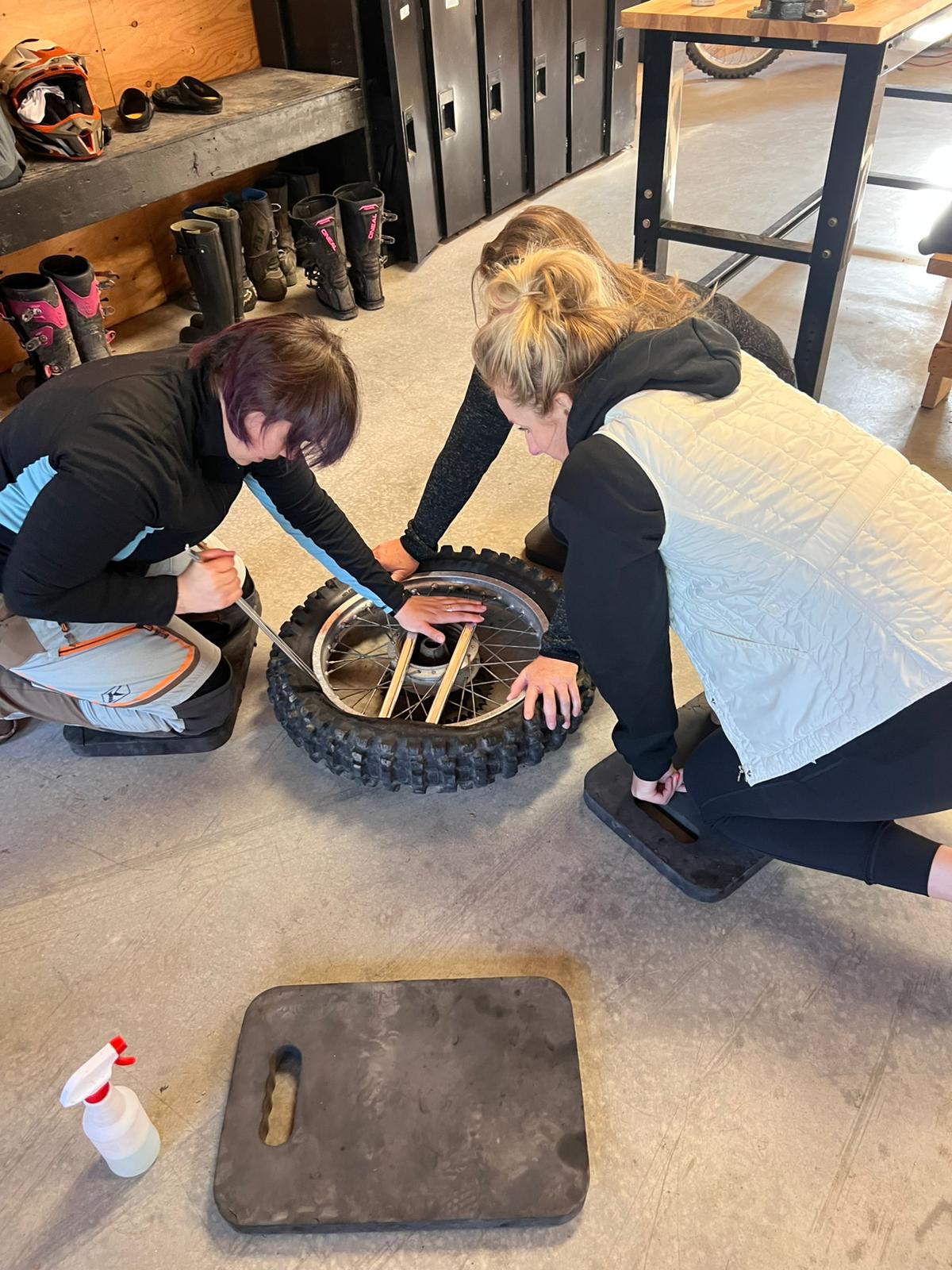 Three individuals working together to repair a motorcycle tire in a workshop, focusing on the tire's inner workings and tools.