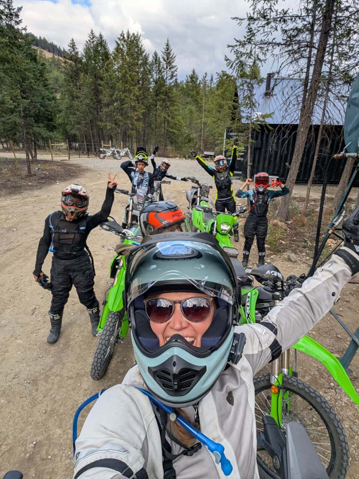 Group of off-road dirt bike riders with helmets and gear posing for a selfie in a forested outdoor area.